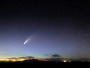 Comet NEOWISE with bright tail in a star-filled sky above mountains and twilight horizon.