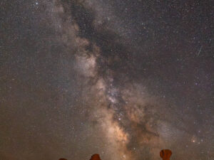 Milky Way stretching across a star-filled sky above illuminated red rock hoodoos in Bryce Canyon.